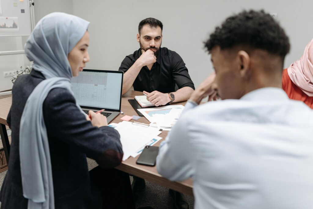 Business professionals engaged in a strategy meeting with laptops and papers in an office setting.